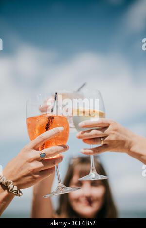 Tre persone stanno tenendo i bicchieri da vino per brindare. I bicchieri sono pieni di bevande di diversi colori, inclusa una bevanda rosa. La scena è celebr Foto Stock