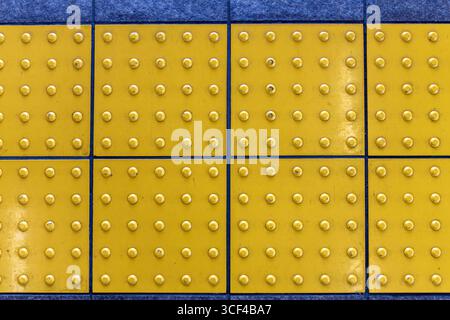 Primo piano di pavimentazione tattile gialla (anche blocchi di tenji, dal nome del braille giapponese) un sistema di indicatori di superficie del terreno testurizzato per aiutare il più piccante Foto Stock