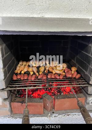Salsicce e pezzetti di pollo grigliati sopra le brace calde su un barbecue tradizionale. Foto Stock