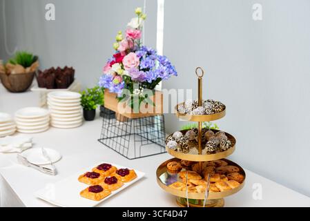 Un sofisticato buffet di dessert con un assortimento di dolci e dolci esposti insieme a una vibrante composizione floreale. perfetto per celeb Foto Stock