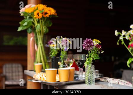 Un vivace giardino estivo con fiori colorati, bevande e spuntini disposti su un tavolo. girasoli luminosi e altri fiori aggiungono un tocco di allegria Foto Stock