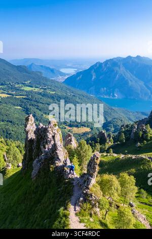 Veduta aerea di un uomo che cammina tra i pinnacoli di roccia sul lato del Colle Pertusio e la valle sotto il Rifugio Rosalba. Piani Resinelli, Lecco, Lombardia, Italia. Foto Stock