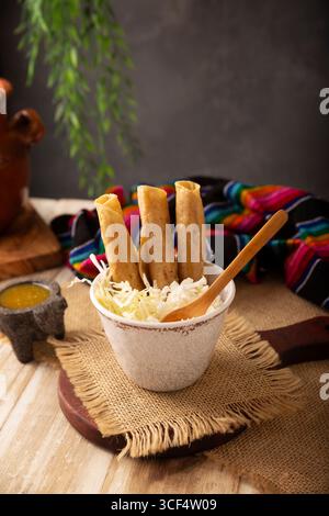Flautas Ahogadas (flautas affogate) Taco dorato fatto con tortillas di mais fritte, ripieni di pollo o manzo, e serviti in un bicchiere o in una tazza contenente S. Foto Stock