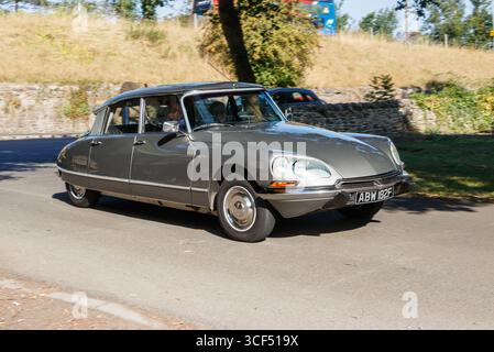 Auto d'epoca grigia da 1968 Citroën DS che guida lungo una strada alberata in una giornata di sole in un ambiente di campagna Foto Stock