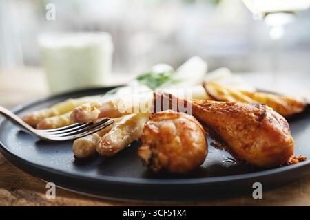 Asparagi bianchi freschi con cosce di pollo arrosto serviti su un piatto di ceramica nera. Sfondo orizzontale per un'alimentazione sana e deliziosa. Primo piano. Foto Stock