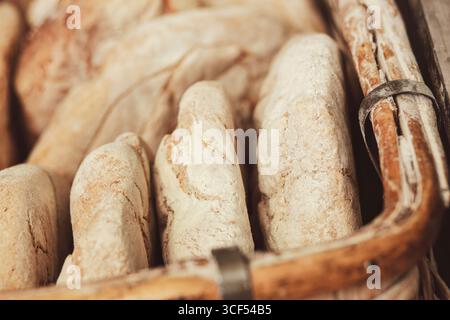 Vista ravvicinata di diverse forme di pane appena sfornato a legna accoccolato in un cesto di vimini, che mette in risalto le loro croste dorate e abbraccia un fascino rustico fatto in casa Foto Stock