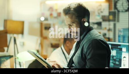 Pensare, tablet e detective in ufficio con digitazione per la ricerca su casi con risoluzione dei problemi. Tecnologia, investigatore privato di notte e uomo con Foto Stock