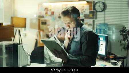 Pensare, detective o uomo con tablet per indagini, approfondimenti o rivedere i lead in ufficio di notte. Tecnico, agente di polizia e pianificazione con prove Foto Stock