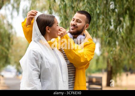 Giovane uomo che copre la testa della sua ragazza con un cappuccio impermeabile nel parco Foto Stock