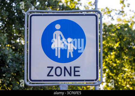 Un segno quadrato indica una zona designata. Il cartello mostra una madre e un bambino che si tengono per mano all'interno di un cerchio blu sopra la parola ZONE Foto Stock