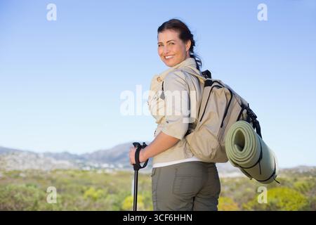 Escursionista donna in piedi su un sentiero collinare che porta zaino con tappetino e bastoncini da trekking, spazio copia Foto Stock