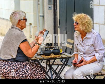 Due donne mature che si scambiano appunti sul proprio smartphone mentre si siedono al tavolino all'aperto nel vecchio quartiere di Tours, Indre-et-Loire (37), Francia. Foto Stock