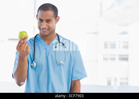 Medico afroamericano maschile in scrub con stetoscopio che tiene la mela verde in clinica, copia spazio Foto Stock