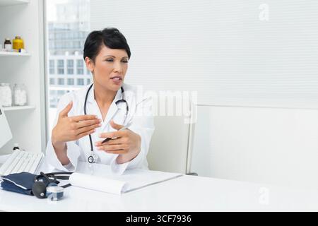 Medico maturo che parla alla scrivania in ufficio indossando camice da laboratorio e spazio di copia dello stetoscopio Foto Stock