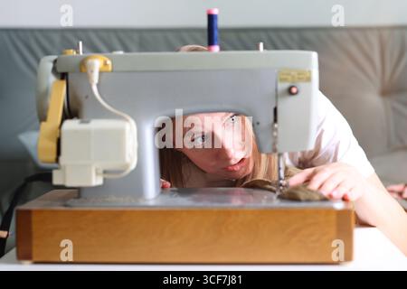 Donna sorpresa che guarda l'ago della macchina da cucire mentre lavora su un tessuto. Foto Stock