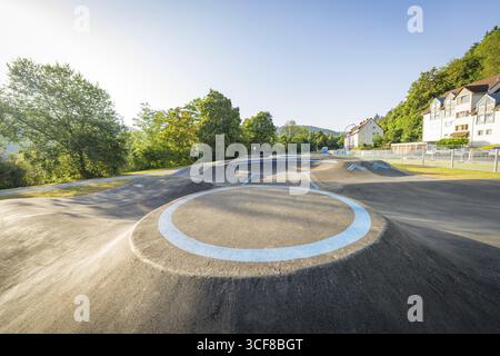 Pista asfaltata curvata con segnaletica blu, circondata da alberi, pista pompa Nagold, distretto di Calw, Germania Foto Stock