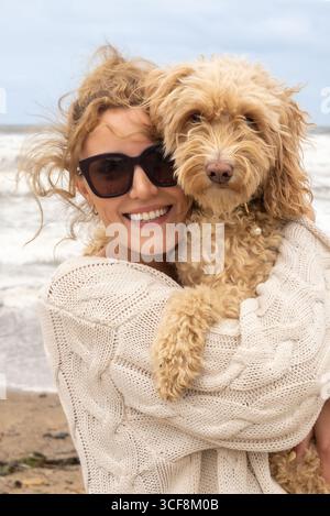 Un ritratto ravvicinato di una donna felice e sorridente e del suo carino cane Cockapoo sulla spiaggia di Saltburn-by-the-Sea nel North Yorkshire, Regno Unito. Foto Stock