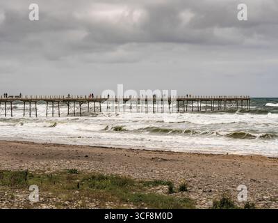 The historic Grade II* listed Victorian pier with people on it, enduring rough waves from the North Sea at Saltburn, North Yorkshire, UK. Foto Stock