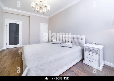 Una camera con una nuova e intima ristrutturazione in tonalità grigio-beige. Ampio letto matrimoniale con coperta grigia. Comodini e un tavolo in stile classico. Foto Stock