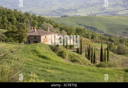 Agriturismo su una dolce collina con cipressi, circondato da una lussureggiante campagna verde e ampie vedute, Toscana, Italia Foto Stock