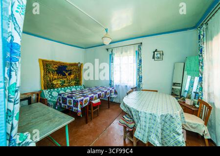 Una stanza in una casa rurale fatiscente. Pareti verdastre, mobili antichi, stoffa d'olio sul tavolo. Tappeto e vecchie foto sul muro. Foto Stock