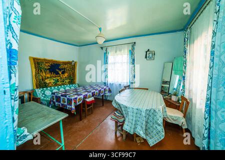 Una stanza in una casa rurale fatiscente. Pareti verdastre, mobili antichi, stoffa d'olio sul tavolo. Tappeto e vecchie foto sul muro. Foto Stock