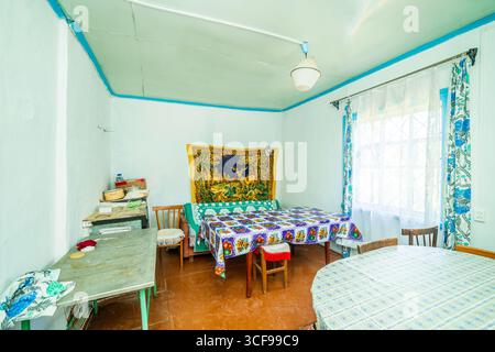 Una stanza in una casa rurale fatiscente. Pareti verdastre, mobili antichi, stoffa d'olio sul tavolo. Tappeto e vecchie foto sul muro. Foto Stock