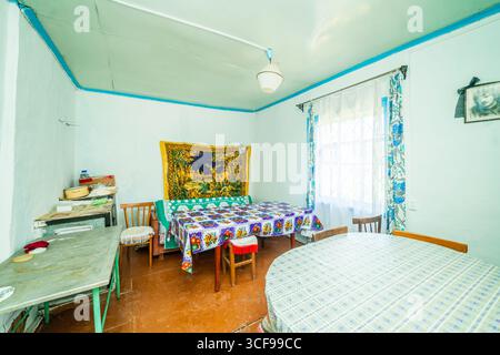 Una stanza in una casa rurale fatiscente. Pareti verdastre, mobili antichi, stoffa d'olio sul tavolo. Tappeto e vecchie foto sul muro. Foto Stock