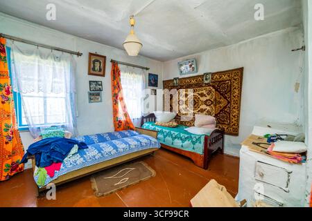 Una stanza in una casa rurale fatiscente. Pareti verdastre, mobili antichi, stoffa d'olio sul tavolo. Tappeto e vecchie foto sul muro. Foto Stock