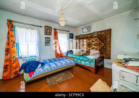 Una stanza in una casa rurale fatiscente. Pareti verdastre, mobili antichi, stoffa d'olio sul tavolo. Tappeto e vecchie foto sul muro. Foto Stock