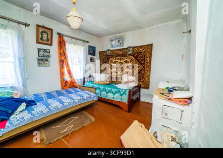 Una stanza in una casa rurale fatiscente. Pareti verdastre, mobili antichi, stoffa d'olio sul tavolo. Tappeto e vecchie foto sul muro. Foto Stock