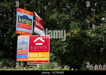 Enfield, Regno Unito 19 agosto 2025 cartelli di più agenti immobiliari raggruppati in un contesto cespuglioso, che rappresentano la vendita di immobili e il marketing immobiliare Foto Stock