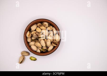 Vista dall'alto verso il basso di un piccolo piatto di terracotta ripieno di pistacchio su sfondo bianco, ideale per illustrare spuntini sani e nutrizione Foto Stock