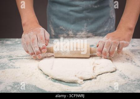 Il panettiere stende l'impasto per pizza, pane piatto o pasticceria con spilla, prepara gli ingredienti per il cibo, cuoci per le feste Foto Stock