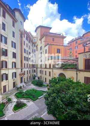 Piante verdi che prosperano tra edifici residenziali, creano un tranquillo paesaggio urbano nel cortile storico di Roma con un delicato sfondo architettonico Foto Stock