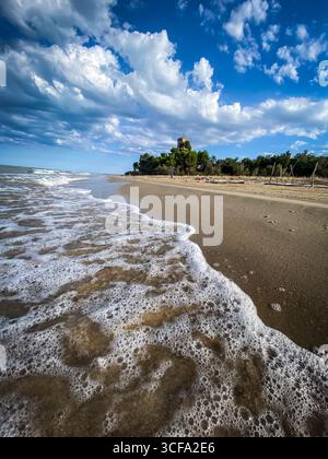 Onde di mare spumeggianti che si infrangono dolcemente sulla spiaggia sabbiosa di Pineto in Abruzzo, con Torre di Cerrano sullo sfondo sotto un bellissimo cielo nuvoloso Foto Stock