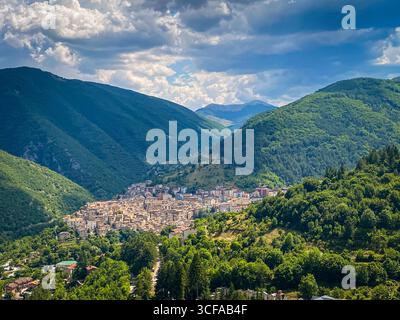 Vista aerea che cattura Scanno annato tra montagne verdeggianti, tradizionali edifici in pietra che punteggiano il paesaggio abruzzese sotto cieli estivi nuvolosi Foto Stock