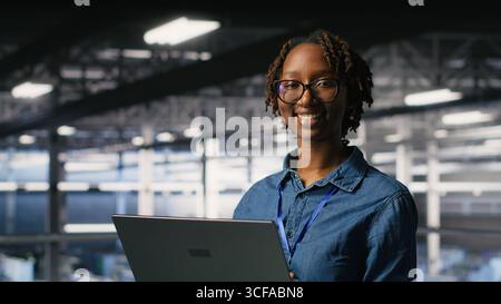 Donna felice nel data center che esegue attività di manutenzione su un notebook, garantendo prestazioni ottimali. Il team di progettazione esamina la diagnostica e applica le patch alla sala server, migliorando la stabilità Foto Stock