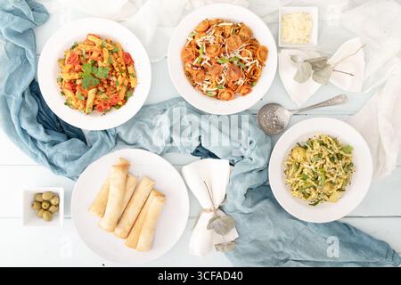Piatto piatto di pasta assortita con antipasti, erbe aromatiche e olive, colorato pasto in stile mediterraneo sullo sfondo bianco e blu. Foto Stock