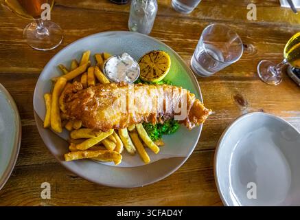 Pasto tradizionale a base di pesce e patatine con piselli moschi, salsa tartara e fetta di limone, ideale per illustrare la cucina britannica, la fotografia gastronomica o tra Foto Stock