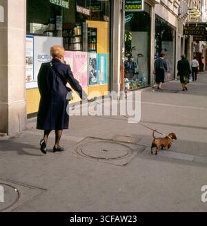 Donna che cammina su un dachshund dai capelli lisci sul marciapiede, passando davanti ai negozi, Parigi, Francia Foto Stock