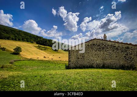 Pittoresco paesaggio caratterizzato da un fienile di pietra e balle di fieno in una soleggiata giornata estiva in Toscana, Italia Foto Stock