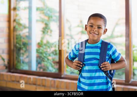 Bambino in piedi su davanzale in mattoni vicino allo zaino che afferrava le finestre e ammirava le piante che arrampicano Foto Stock