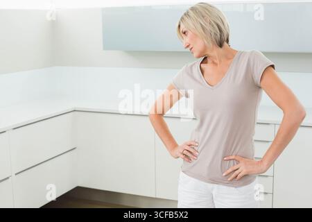 Donna di mezza età in piedi in una cucina moderna con armadi bianchi e piano di lavoro, spazio fotocopie Foto Stock