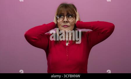 Donna in maglione rosso con le mani sulla testa su sfondo rosa che appare premurosa o preoccupata Foto Stock