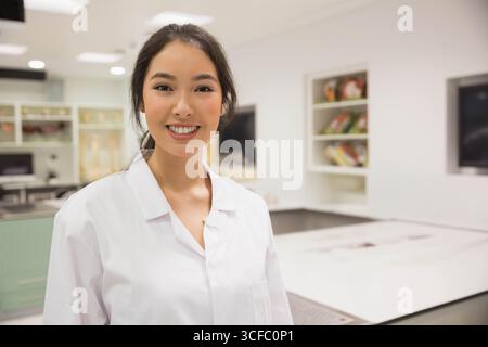 Scienziata asiatica sorridente in classe di laboratorio accanto a banchi di laboratorio e modelli di scheletro Foto Stock