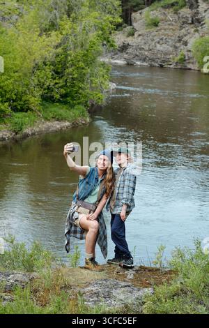 Famiglia che porta Selfie insieme all'aperto vicino al fiume Foto Stock