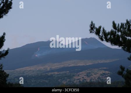 Nell'agosto del 2025 l'Etna entrò in una fase effusiva alimentata da bocche tra bocca nuova e il cratere sudorientale a 2.980–3.200 m s.l.m., inviando freschi corsi di lava lungo la base del cratere sudorientale e sui fianchi sudovest/occidentali superiori. Le immagini mostrano turisti curiosi e gruppi guidati che osservano i flussi luminosi e le esplosioni stromboliane intermittenti al cratere sudorientale, con piccole scogliere di cenere e pennacchi di gas che si disperdono rapidamente. Altri sfiati annotati il 20 e il 21 agosto, con flussi che avanzano da sud a sud-ovest attraverso l'area della cima. Foto Stock