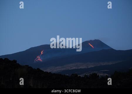Nell'agosto del 2025 l'Etna entrò in una fase effusiva alimentata da bocche tra bocca nuova e il cratere sudorientale a 2.980–3.200 m s.l.m., inviando freschi corsi di lava lungo la base del cratere sudorientale e sui fianchi sudovest/occidentali superiori. Le immagini mostrano turisti curiosi e gruppi guidati che osservano i flussi luminosi e le esplosioni stromboliane intermittenti al cratere sudorientale, con piccole scogliere di cenere e pennacchi di gas che si disperdono rapidamente. Altri sfiati annotati il 20 e il 21 agosto, con flussi che avanzano da sud a sud-ovest attraverso l'area della cima. Foto Stock