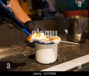 uomo che brucia marshmallow per una cioccolata calda in un caffè Foto Stock